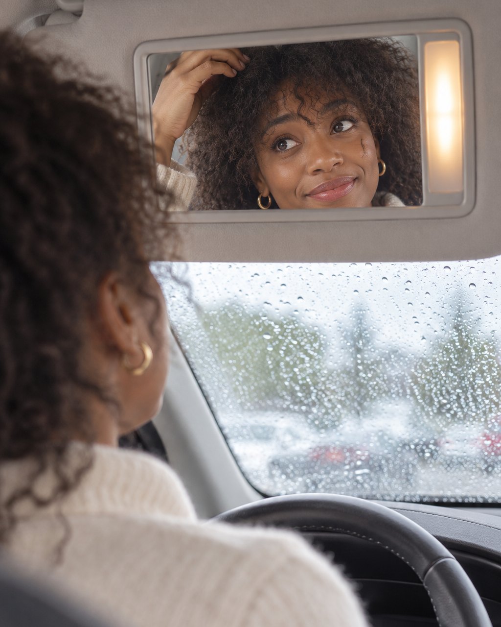Woman in a parked car checking her frizzy fringe in the visor mirror on a rainy day