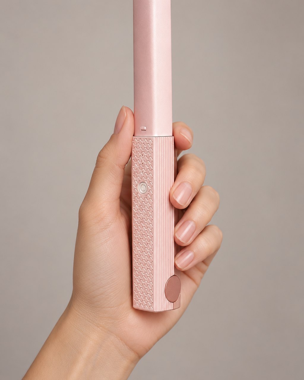 The closed pink mini flat iron held upright in one hand, showing its slim size