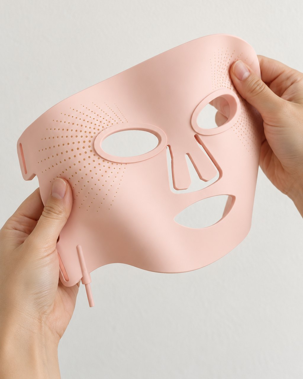 Silicone LED mask held in two hands and gently bent to show how flexible it is