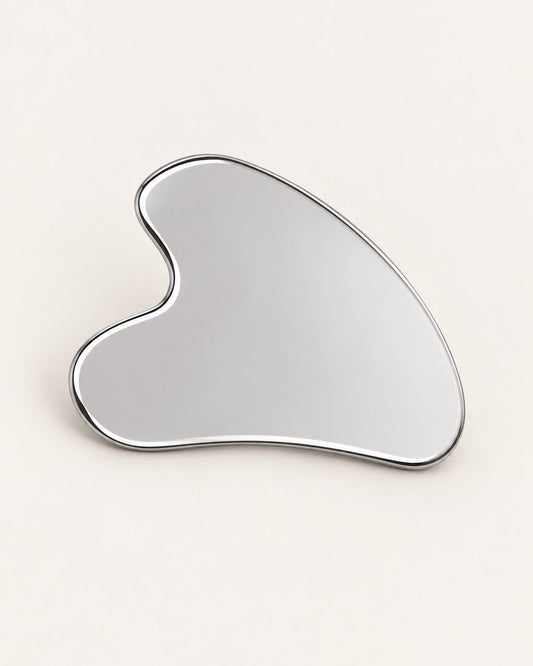 Heart-shaped stainless steel gua sha with a mirror finish on a light background