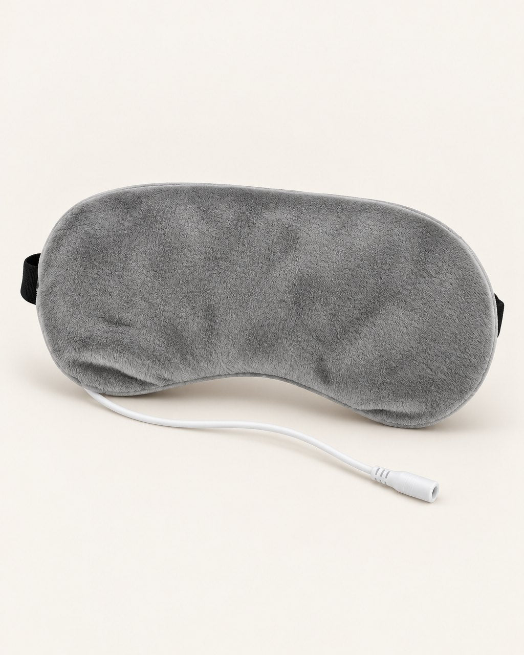 Grey plush heated eye mask with its USB cable on a light background