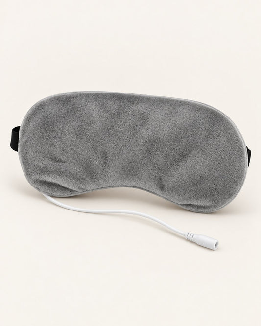 Grey plush heated eye mask with its USB cable on a light background