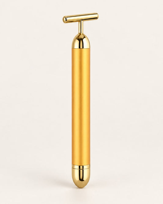 Gold-tone vibrating beauty bar with a T-shaped head, standing upright on a light background